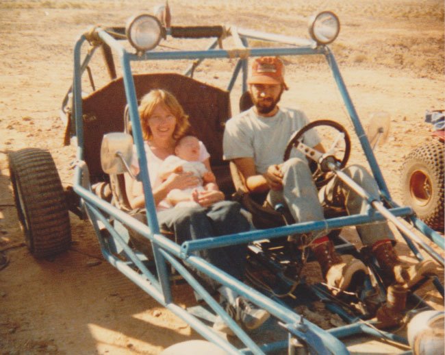 Man and woman in dune buggy with baby Aaron, on a desert backdrop